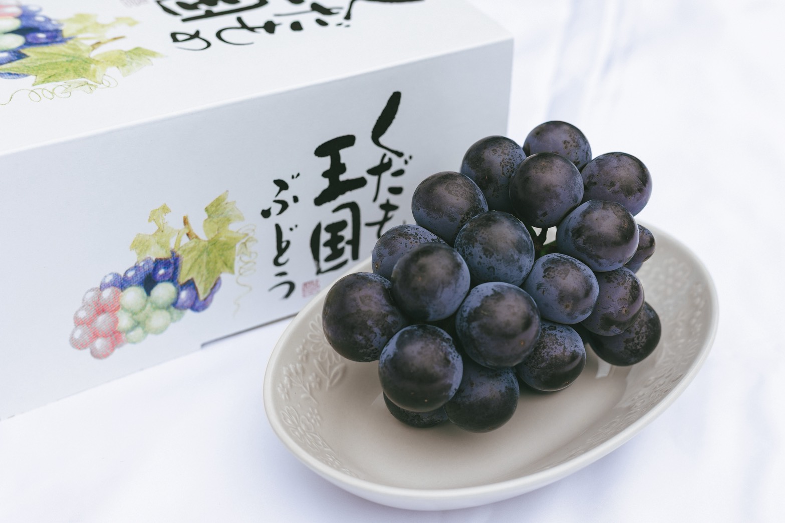 化粧箱のとなりに、皿へ盛った粉のふいたピオーネの房