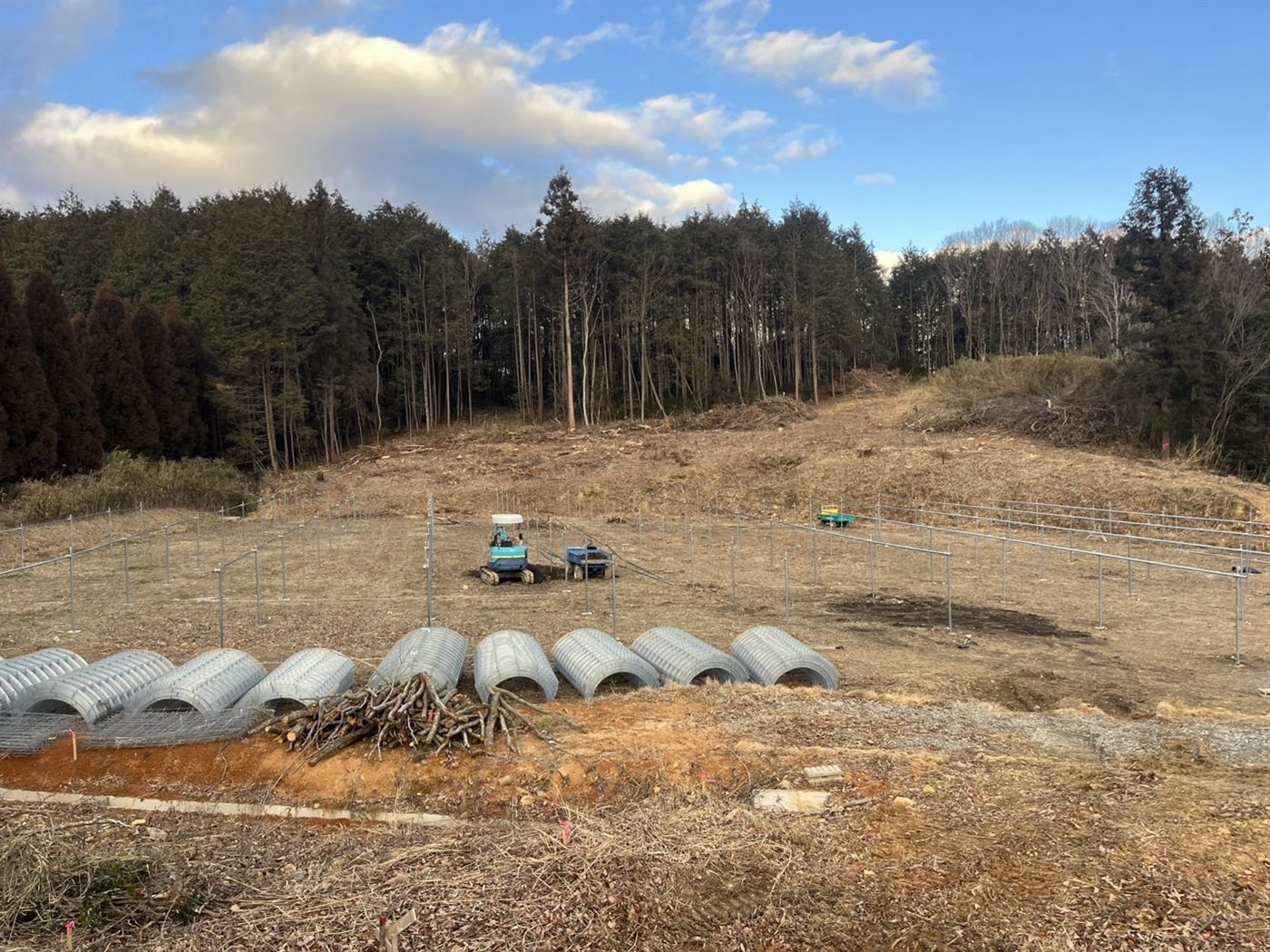重機で土をならし、管を並べ、柱を立てはじめた造成中の畑